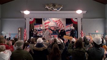 Movie still from “The Dead Zone” (1983), directed by David Cronenberg – A group of people standing in front of an american flag; Wide shot, High angle