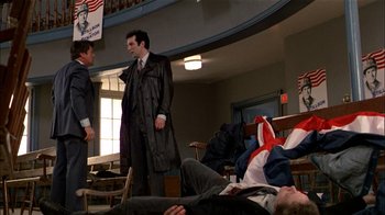 Movie still from “The Dead Zone” (1983), directed by David Cronenberg – Two men in suits stand in front of a man lying on the floor; Wide shot, Low angle
