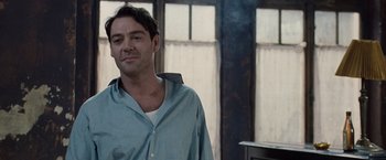 Movie still from “The Debt” (2010), directed by John Madden – A man standing in front of a window with smoke coming out of the window; Medium shot, Over the shoulder angle