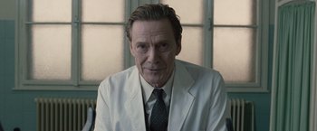 Movie still from “The Debt” (2010), directed by John Madden – A person wearing a suit and tie; Close Up shot, Low angle