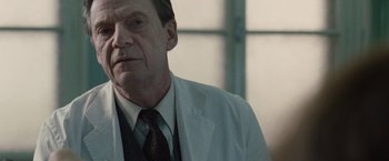 Movie still from “The Debt” (2010), directed by John Madden – An older man in a white lab coat and tie; Close Up shot, Over the shoulder angle