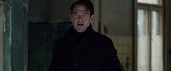 Movie still from “The Debt” (2010), directed by John Madden – A man in a black jacket is standing in a dark room; Close Up shot, Low angle