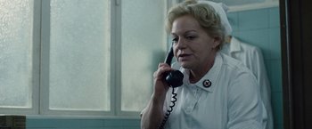 Movie still from “The Debt” (2010), directed by John Madden – An older woman talking on a phone while wearing a nurse's uniform; Close Up shot, Low angle