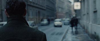 Movie still from “The Debt” (2010), directed by John Madden – A man standing on a street next to a busy street; Close Up shot, Over the shoulder angle