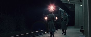 Movie still from “The Debt” (2010), directed by John Madden – A man in a uniform is standing on a train platform; Wide shot, Low angle