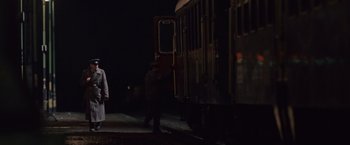 Movie still from “The Debt” (2010), directed by John Madden – A man standing next to a train on a train track at night; Wide shot, Over the shoulder angle