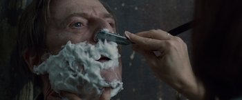 Movie still from “The Debt” (2010), directed by John Madden – A person shaving a man's face with a razor; Extreme Close Up shot, Over the shoulder angle