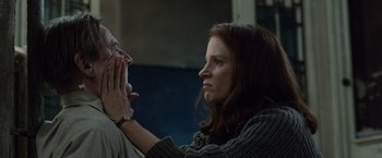 Movie still from “The Debt” (2010), directed by John Madden – A woman sitting next to a man holding his hand up; Close Up shot, Low angle