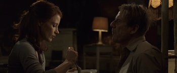 Movie still from “The Debt” (2010), directed by John Madden – A man and a woman holding hands over a plate; Medium shot, Over the shoulder angle