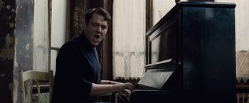 Movie still from “The Debt” (2010), directed by John Madden – A man in a black shirt is playing the piano; Medium shot, Low angle
