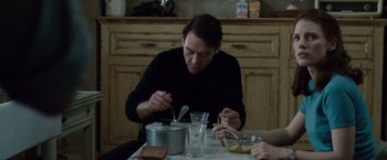 Movie still from “The Debt” (2010), directed by John Madden – A man sitting at a table with a bowl of food; Medium shot, Over the shoulder angle