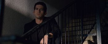 Movie still from “The Debt” (2010), directed by John Madden – A man standing next to a railing in a dark room; Medium shot, Low angle