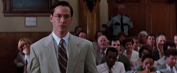Movie still from “The Devil's Advocate” (1997), directed by Taylor Hackford – A man in a suit and tie standing in front of a group of people; Close Up shot, Low angle