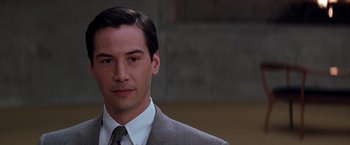 Movie still from “The Devil's Advocate” (1997), directed by Taylor Hackford – A man wearing a suit and tie in front of a building; Close Up shot, Over the shoulder angle