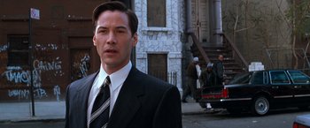 Movie still from “The Devil's Advocate” (1997), directed by Taylor Hackford – A man wearing a suit and tie standing on a sidewalk; Close Up shot, Over the shoulder angle