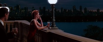 Movie still from “The Devil's Advocate” (1997), directed by Taylor Hackford – A woman in a red dress sitting on a ledge with a glass of wine; Medium shot, Low angle