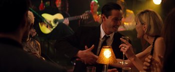 Movie still from “The Devil's Advocate” (1997), directed by Taylor Hackford – A man sitting at a table with a lamp in front of him; Medium shot, Over the shoulder angle
