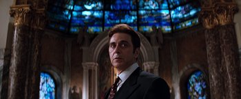 Movie still from “The Devil's Advocate” (1997), directed by Taylor Hackford – A man in a suit and tie in front of a stained glass window; Medium shot, Low angle