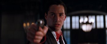 Movie still from “The Devil's Advocate” (1997), directed by Taylor Hackford – A man in a suit and tie holding a gun in his hand; Close Up shot, Low angle