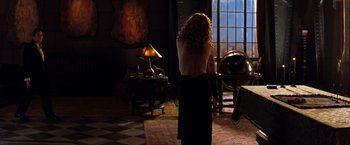Movie still from “The Devil's Advocate” (1997), directed by Taylor Hackford – A woman standing in front of a window in a dark room; Medium shot, Over the shoulder angle