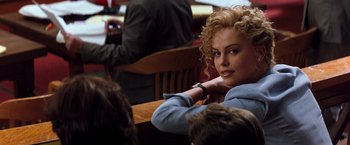 Movie still from “The Devil's Advocate” (1997), directed by Taylor Hackford – A woman sitting at a wooden table with her hand on her chin; Close Up shot, Over the shoulder angle