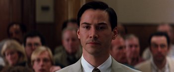Movie still from “The Devil's Advocate” (1997), directed by Taylor Hackford – A man in a suit and tie in front of a group of people; Close Up shot, Over the shoulder angle