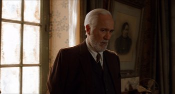 Movie still from “The Devil's Backbone” (2001), directed by Guillermo del Toro – An older man in a suit and tie in front of a painting; Medium shot, Over the shoulder angle