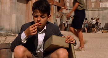 Movie still from “The Devil's Backbone” (2001), directed by Guillermo del Toro – A young boy sitting on the ground eating something; Medium shot, Low angle