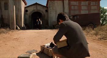 Movie still from “The Devil's Backbone” (2001), directed by Guillermo del Toro – A man sitting on the side of the road next to an open briefcase; Wide shot, Over the shoulder angle