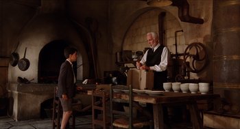 Movie still from “The Devil's Backbone” (2001), directed by Guillermo del Toro – An older man and a young boy standing in front of a table; Medium shot, Over the shoulder angle