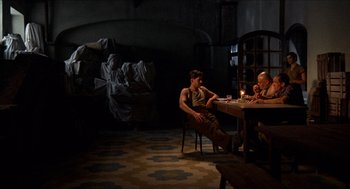 Movie still from “The Devil's Backbone” (2001), directed by Guillermo del Toro – A man sitting at a table in a dark room; Wide shot, High angle