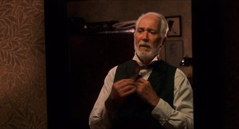 Movie still from “The Devil's Backbone” (2001), directed by Guillermo del Toro – An older man adjusting his neck tie in a room; Close Up shot, Low angle