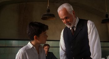 Movie still from “The Devil's Backbone” (2001), directed by Guillermo del Toro – A man in a suit and tie standing next to a young boy; Medium shot, Over the shoulder angle
