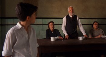 Movie still from “The Devil's Backbone” (2001), directed by Guillermo del Toro – A man and a woman sitting at a table with a young boy standing next to them; Medium shot, Over the shoulder angle