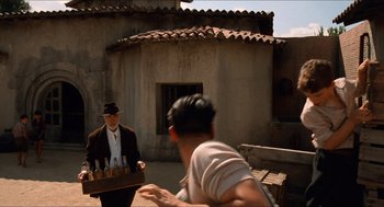 Movie still from “The Devil's Backbone” (2001), directed by Guillermo del Toro – A man in a hat is holding a crate; Wide shot, Over the shoulder angle
