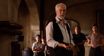 Movie still from “The Devil's Backbone” (2001), directed by Guillermo del Toro – An older man holding a gun while standing in front of a group of people; Medium shot, Low angle