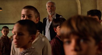 Movie still from “The Devil's Backbone” (2001), directed by Guillermo del Toro – An older man standing in front of a group of young boys; Medium shot, Over the shoulder angle