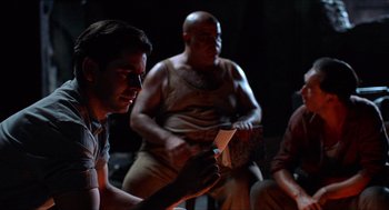Movie still from “The Devil's Backbone” (2001), directed by Guillermo del Toro – A group of men sitting in a dark room holding papers; Medium shot, Over the shoulder angle