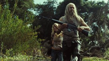 Movie still from “The Devil's Rejects” (2005), directed by Rob Zombie – A man and a woman holding a rifle in a forest; Medium shot, Low angle