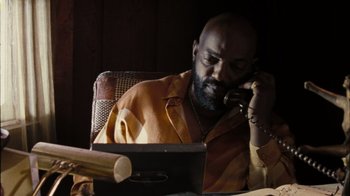 Movie still from “The Devil's Rejects” (2005), directed by Rob Zombie – A man sitting at a table talking on a phone; Medium shot, High angle