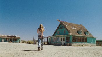 Movie still from “The Devil's Rejects” (2005), directed by Rob Zombie – A woman riding a scooter down a dirt road near a house; Wide shot, Low angle
