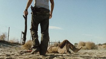 Movie still from “The Devil's Rejects” (2005), directed by Rob Zombie – A man standing next to another man laying on the ground; Wide shot, Low angle