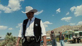 Movie still from “The Devil's Rejects” (2005), directed by Rob Zombie – A man wearing a white cowboy hat and a black vest; Medium shot, Over the shoulder angle
