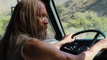 Movie still from “The Devil's Rejects” (2005), directed by Rob Zombie – A man with long hair driving a car in the mountains; Close Up shot, Over the shoulder angle