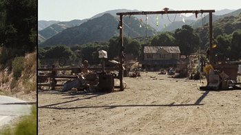 Movie still from “The Devil's Rejects” (2005), directed by Rob Zombie – An outdoor area with people sitting on the ground and a building in the background; Extreme Wide shot, High angle