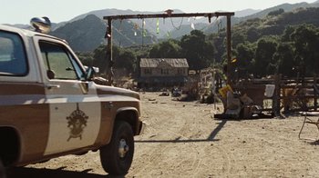 Movie still from “The Devil's Rejects” (2005), directed by Rob Zombie – A truck parked in a dirt field near a building; Wide shot, Low angle