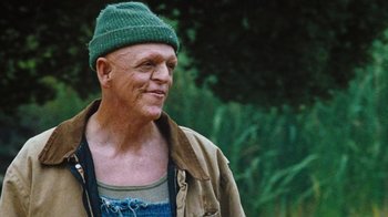 Movie still from “The Devil's Rejects” (2005), directed by Rob Zombie – An older man wearing a green hat is smiling for the camera; Medium shot, Low angle