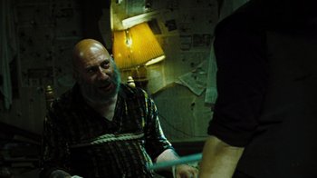 Movie still from “The Devil's Rejects” (2005), directed by Rob Zombie – An old man with a beard is tied up; Medium shot, Over the shoulder angle