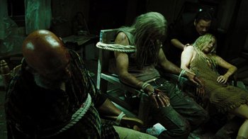 Movie still from “The Devil's Rejects” (2005), directed by Rob Zombie – A group of people sitting in a dark room; Medium shot, High angle