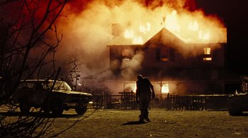 Movie still from “The Devil's Rejects” (2005), directed by Rob Zombie – A person walking in front of a house on fire; Wide shot, Low angle